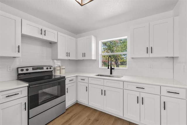 kitchen with electric stove, light countertops, light wood-style flooring, white cabinetry, and a sink