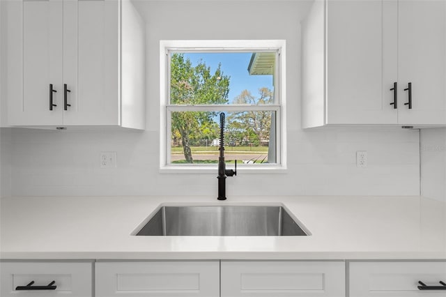 kitchen featuring tasteful backsplash, light countertops, a sink, and white cabinetry