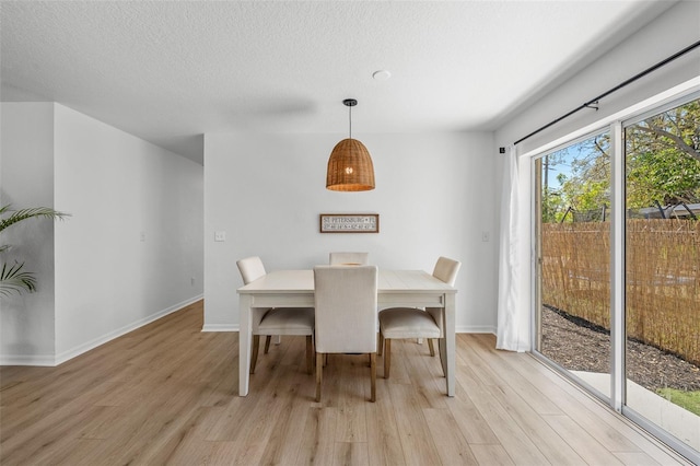 dining room featuring baseboards, light wood-style flooring, and a textured ceiling