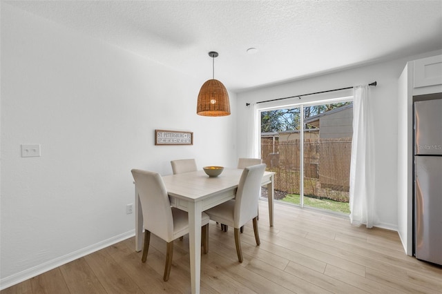 dining area with light wood-type flooring, baseboards, and a textured ceiling