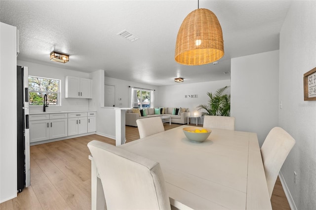 dining space with light wood-type flooring, baseboards, visible vents, and a textured ceiling