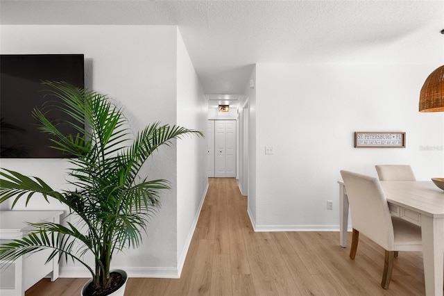 hall featuring baseboards, a textured ceiling, and light wood finished floors