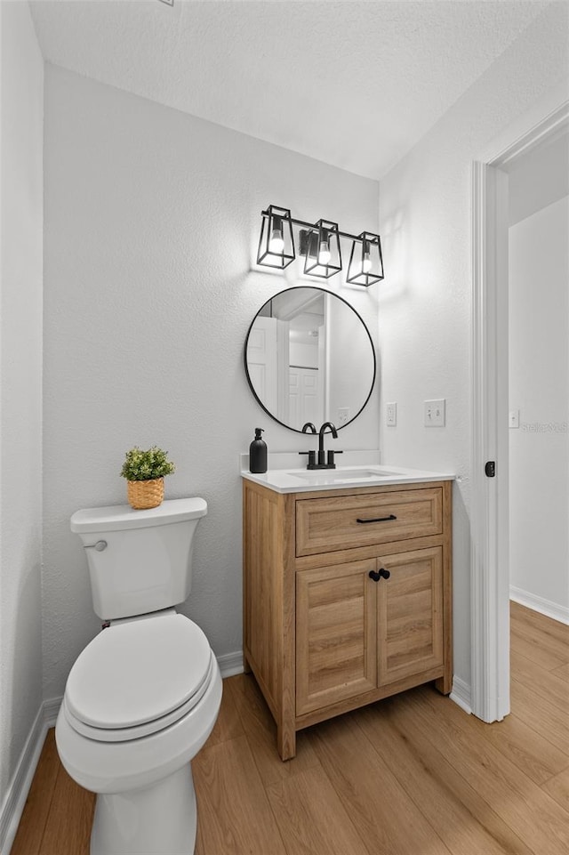 half bath featuring toilet, baseboards, wood finished floors, and vanity