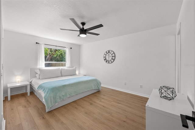 bedroom featuring light wood-style floors, ceiling fan, baseboards, and a textured ceiling