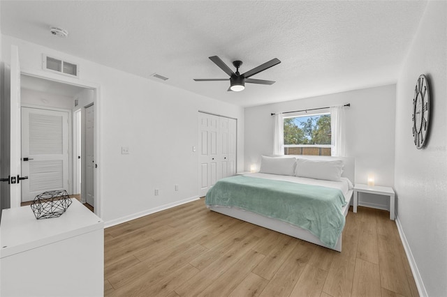 bedroom with light wood finished floors, baseboards, visible vents, and a textured ceiling