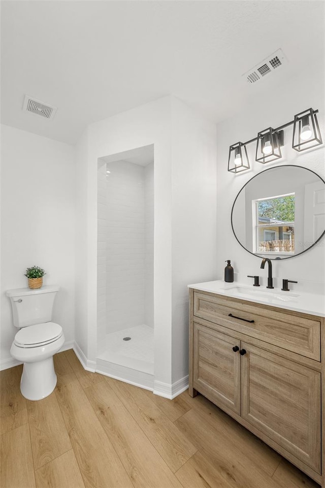 bathroom with visible vents, tiled shower, toilet, and wood finished floors