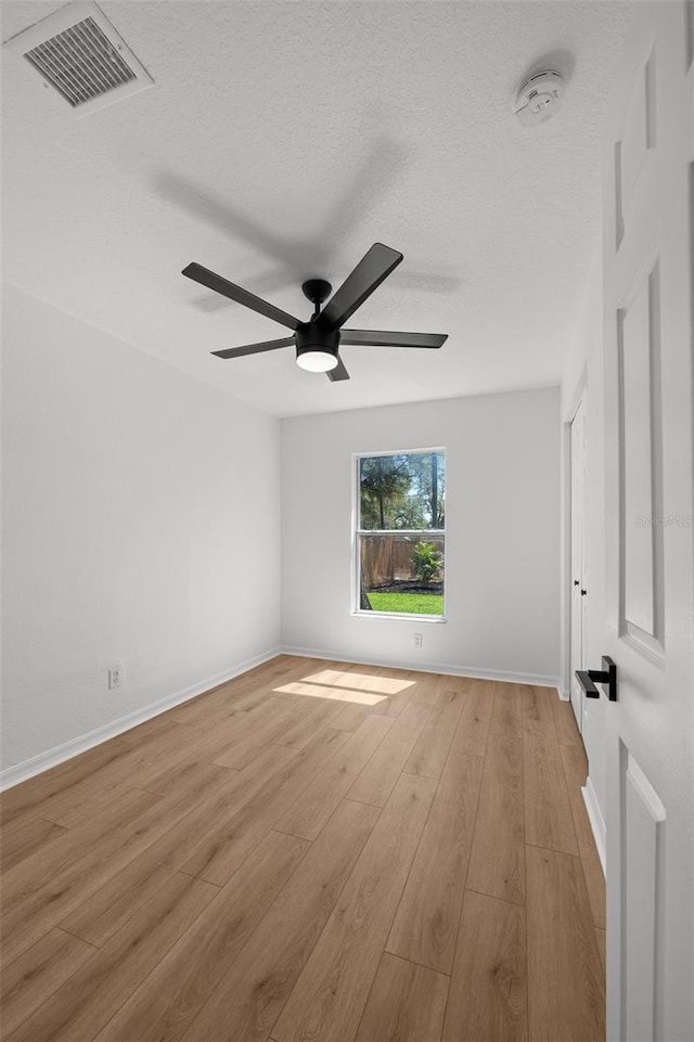 spare room featuring visible vents, light wood-style floors, ceiling fan, a textured ceiling, and baseboards