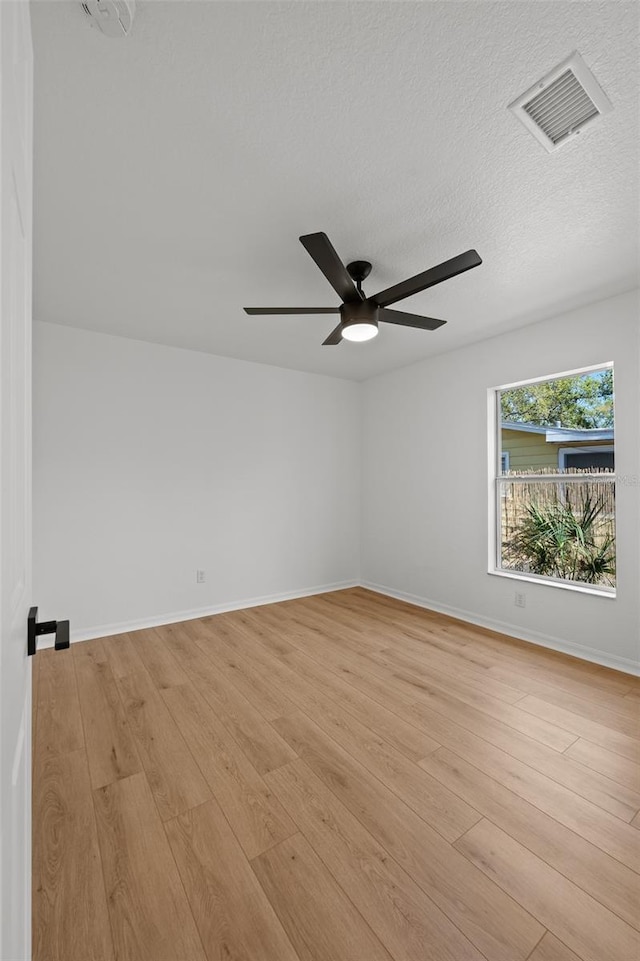 spare room featuring a textured ceiling, a ceiling fan, baseboards, visible vents, and light wood-style floors