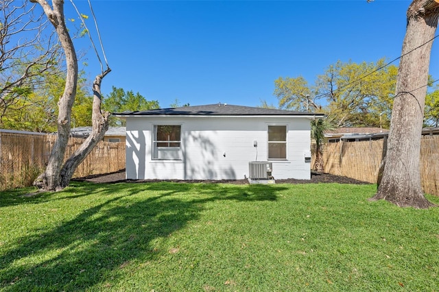 rear view of house with a fenced backyard, central AC unit, and a lawn