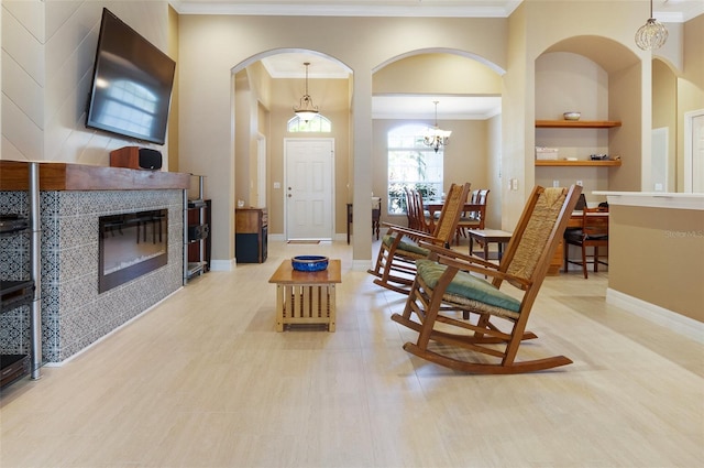 living area with crown molding, built in shelves, baseboards, and a tiled fireplace