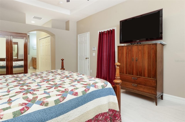 bedroom with arched walkways, ceiling fan, visible vents, baseboards, and ensuite bath