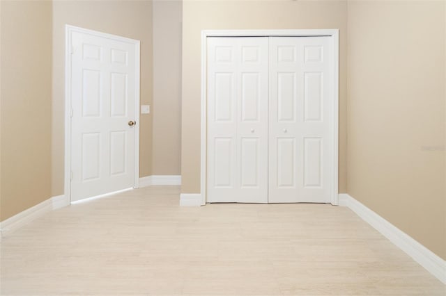 unfurnished bedroom featuring light wood-type flooring, a closet, and baseboards