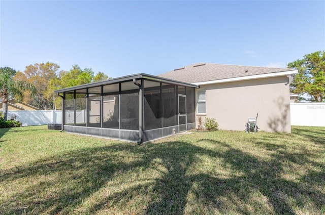 rear view of house featuring a sunroom, fence, stucco siding, and a yard