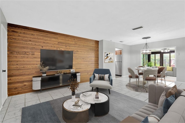 living room with wooden walls, a notable chandelier, an accent wall, visible vents, and baseboards