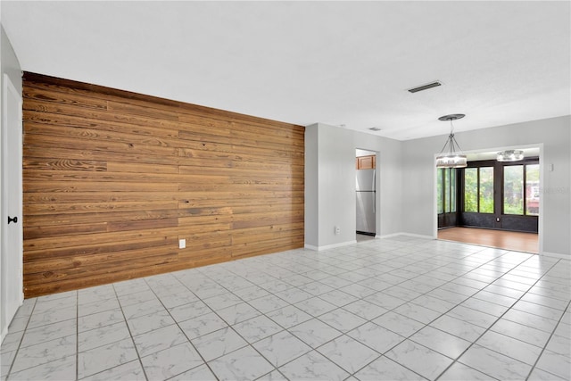 empty room featuring a notable chandelier, an accent wall, wood walls, visible vents, and baseboards