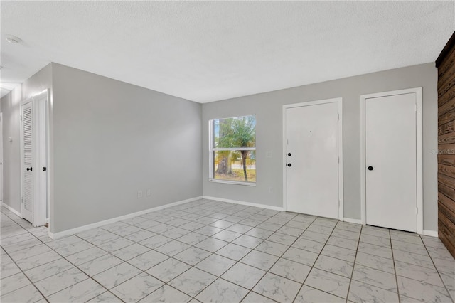 empty room with marble finish floor, baseboards, and a textured ceiling