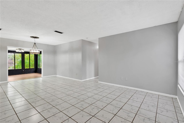 spare room featuring a textured ceiling, baseboards, visible vents, and a notable chandelier