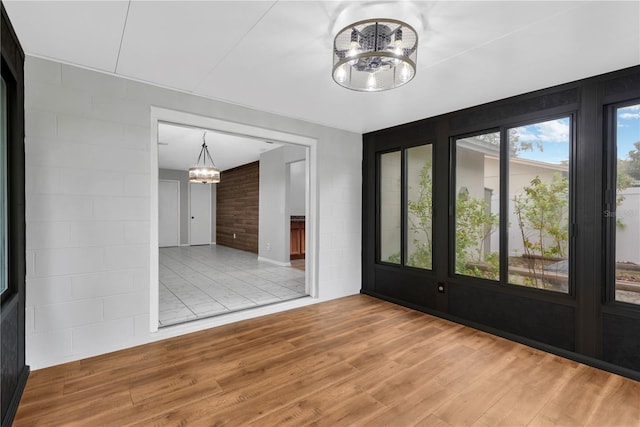 unfurnished room with a chandelier, wood finished floors, and concrete block wall