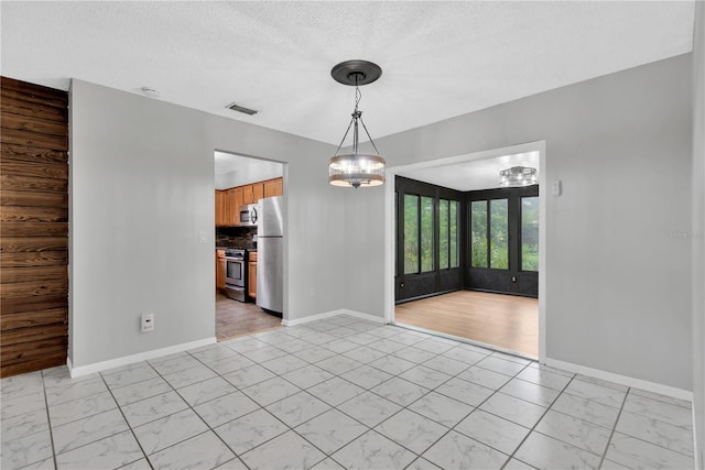 unfurnished room with marble finish floor, visible vents, an inviting chandelier, a textured ceiling, and baseboards