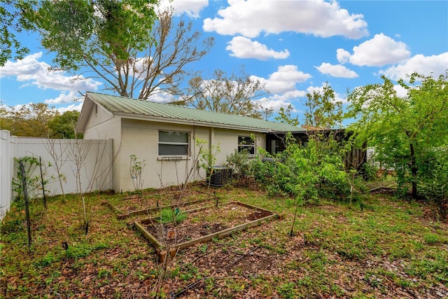 rear view of house with metal roof, central air condition unit, concrete block siding, fence, and a vegetable garden