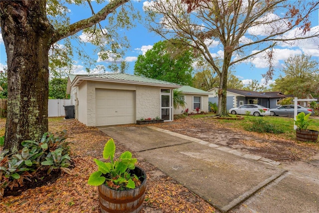 single story home with metal roof, an attached garage, fence, concrete block siding, and concrete driveway