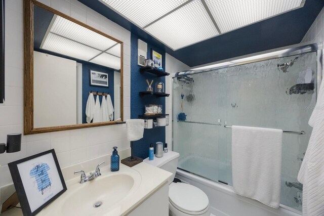 bathroom with toilet, enclosed tub / shower combo, backsplash, vanity, and tile walls