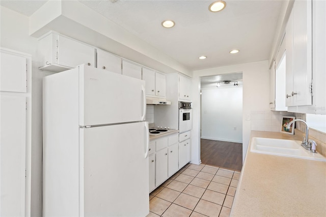 kitchen featuring light countertops, backsplash, a sink, white appliances, and under cabinet range hood