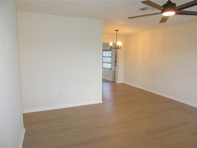 spare room featuring ceiling fan with notable chandelier, wood finished floors, visible vents, and baseboards