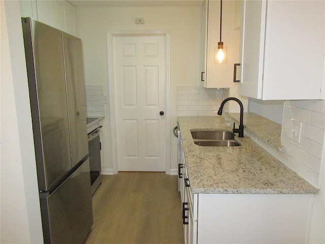 kitchen with tasteful backsplash, appliances with stainless steel finishes, white cabinetry, a sink, and wood finished floors