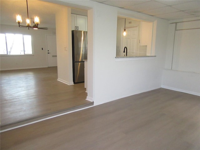 unfurnished room with a chandelier, dark wood-type flooring, a drop ceiling, and baseboards