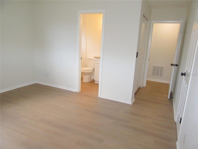 unfurnished bedroom featuring light wood-type flooring, connected bathroom, visible vents, and baseboards