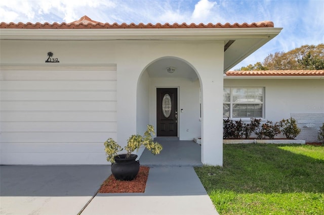 view of exterior entry with a lawn, an attached garage, and stucco siding