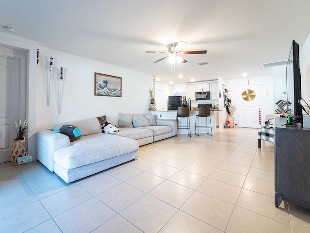 living room featuring light tile patterned floors, visible vents, a textured ceiling, and a ceiling fan