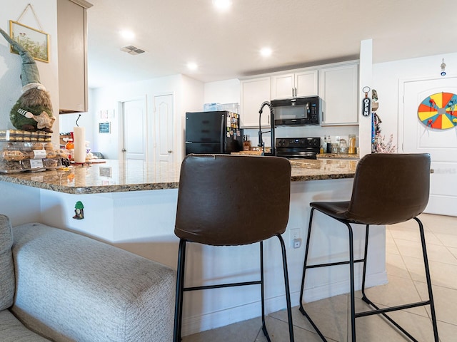 kitchen with visible vents, light tile patterned floors, dark stone countertops, a kitchen breakfast bar, and black appliances