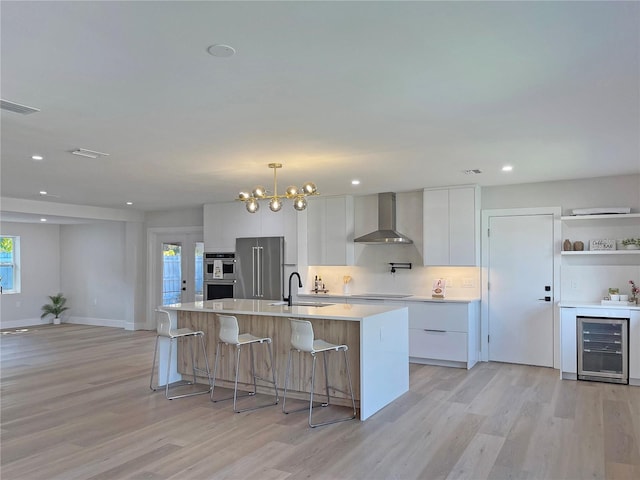 kitchen featuring visible vents, wine cooler, white cabinets, stainless steel appliances, and wall chimney exhaust hood