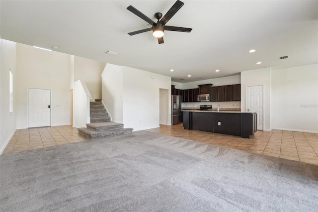 unfurnished living room featuring light tile patterned floors, visible vents, ceiling fan, stairs, and light colored carpet