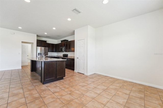 kitchen with light stone counters, a center island with sink, recessed lighting, dark brown cabinetry, and appliances with stainless steel finishes