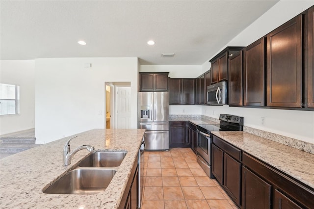 kitchen featuring dark brown cabinets, light stone countertops, light tile patterned floors, appliances with stainless steel finishes, and a sink