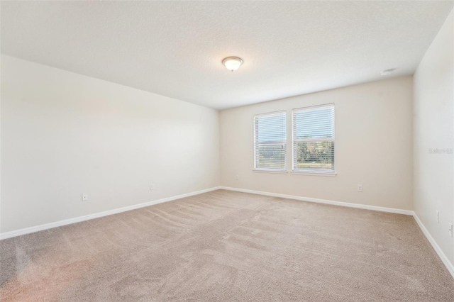 empty room featuring a textured ceiling, baseboards, and light carpet