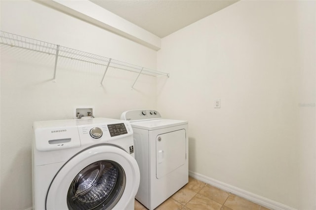 clothes washing area with laundry area, light tile patterned flooring, washing machine and dryer, and baseboards