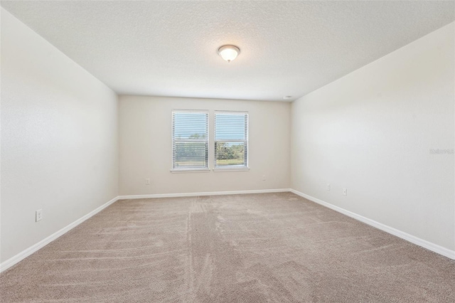 spare room with a textured ceiling, baseboards, and light carpet