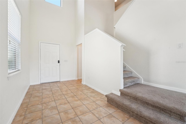 entrance foyer with light tile patterned floors, stairway, baseboards, and a high ceiling