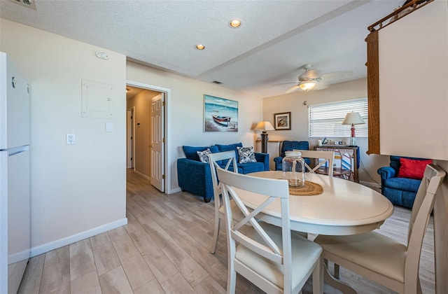 dining area featuring light wood finished floors, baseboards, visible vents, a ceiling fan, and a textured ceiling