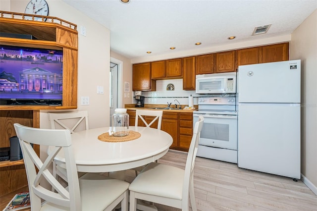 kitchen featuring light wood-style flooring, white appliances, visible vents, decorative backsplash, and brown cabinets