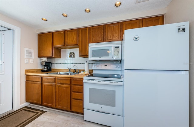 kitchen featuring white appliances, brown cabinetry, and a sink