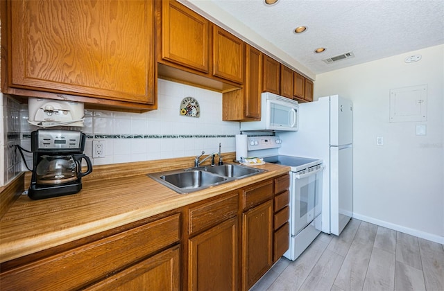 kitchen featuring visible vents, backsplash, brown cabinetry, a sink, and white appliances