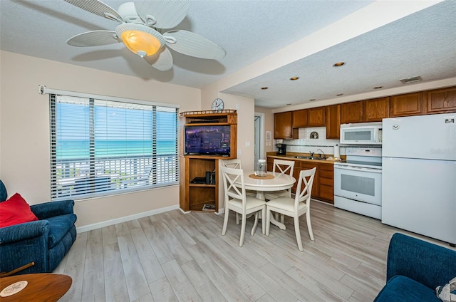 kitchen featuring white appliances, light wood finished floors, a textured ceiling, and brown cabinetry