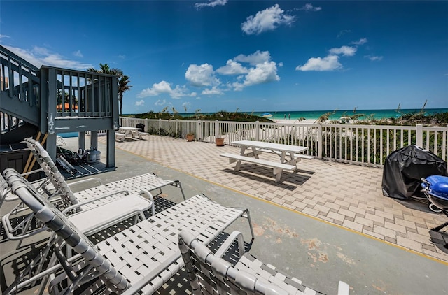 view of patio / terrace featuring a water view, area for grilling, a view of the beach, and outdoor dining space