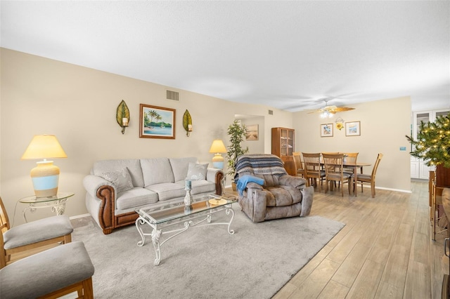 living room featuring a ceiling fan, visible vents, light wood-style flooring, and baseboards