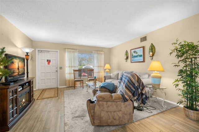 living room featuring visible vents, a textured ceiling, baseboards, and wood finished floors